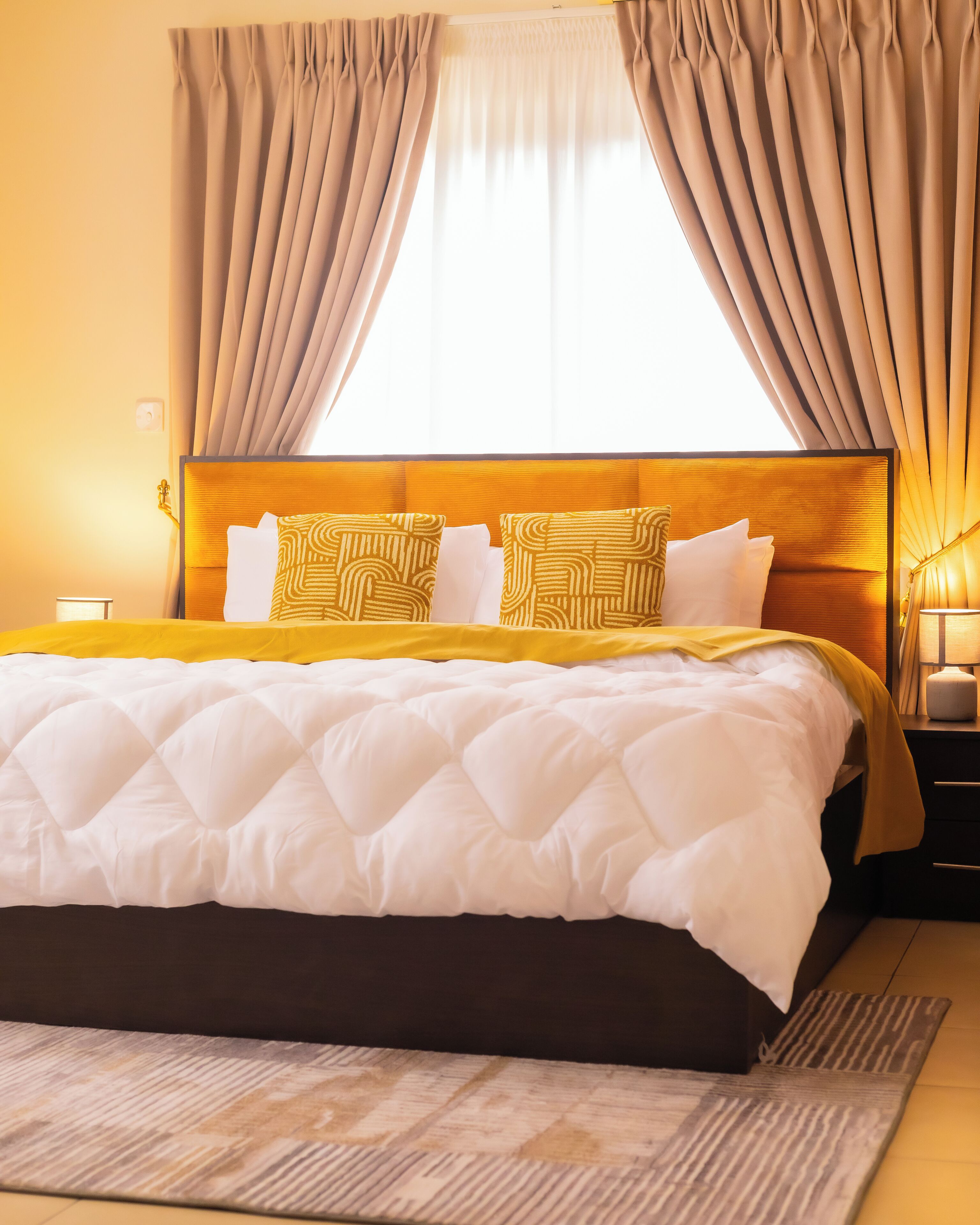 A hotel room with a large bed, beige curtains, and a wooden headboard.