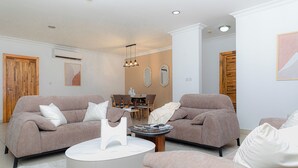A modern living room with two sofas, a coffee table, and a dining area with chairs and a table. - Polo Heights -Sky Suites (Accra)