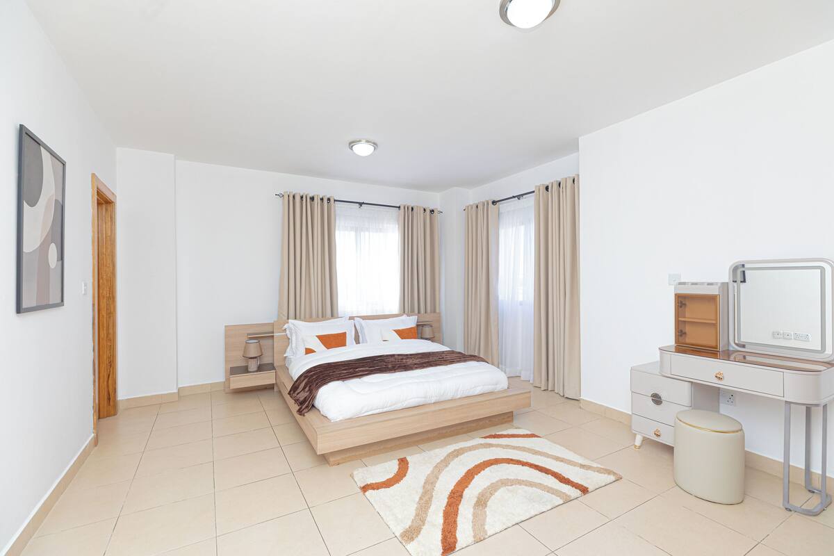 A modern bedroom with a bed, a vanity with a mirror, and a small stool.