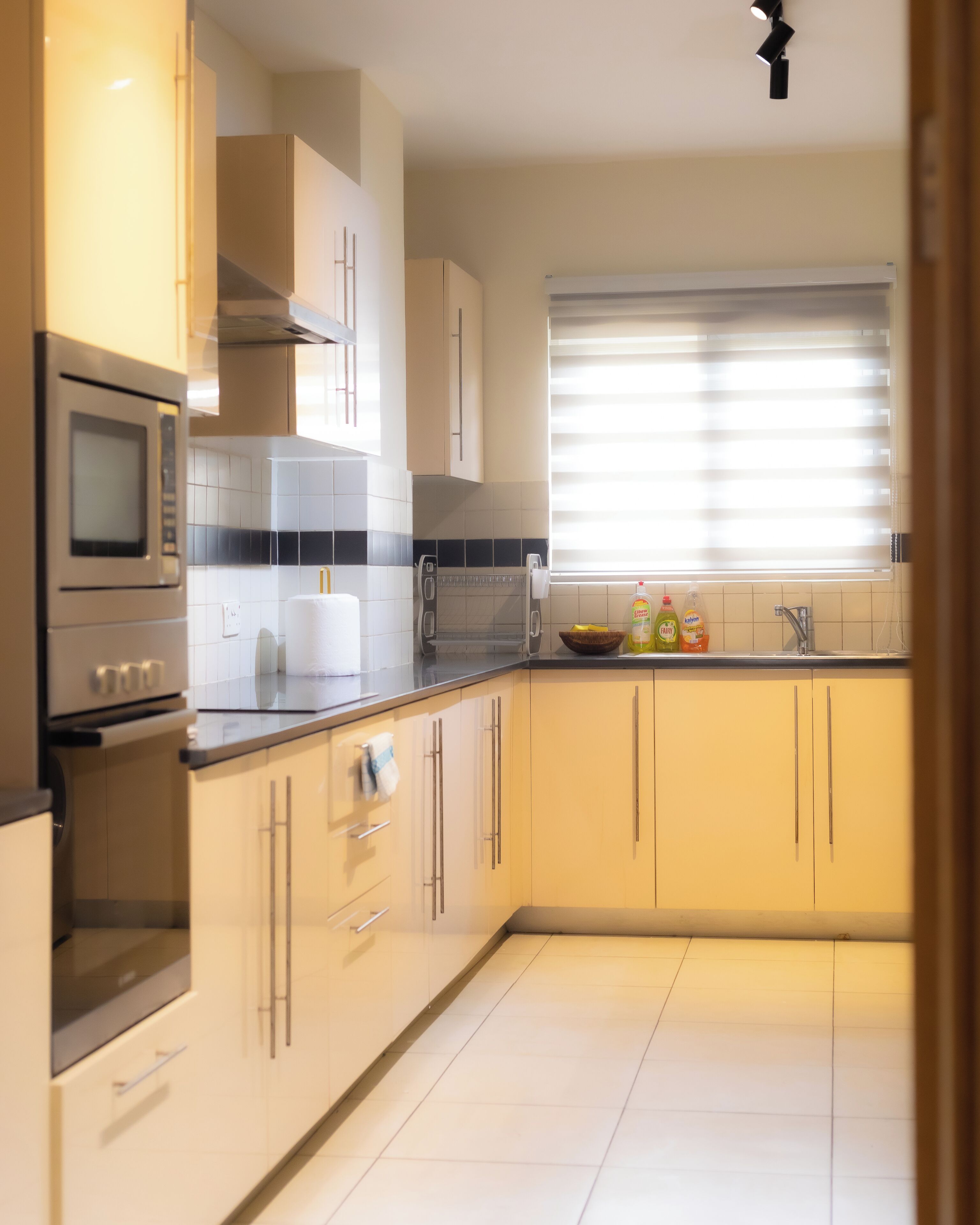 Eine moderne Küche mit Edelstahlgeräten, weißen Schränken und einem Fenster mit Jalousien.