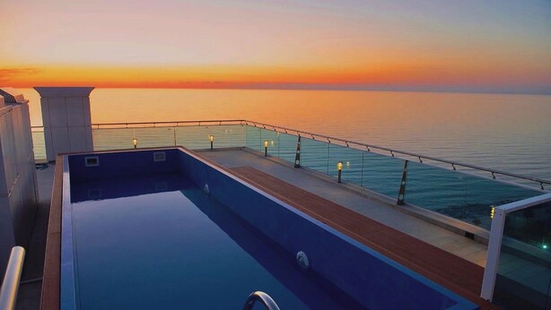 A swimming pool on a deck with a glass railing, overlooking a body of water during sunset. - Apartment with Sea View in New Boulevard of Batumi (Batumi)