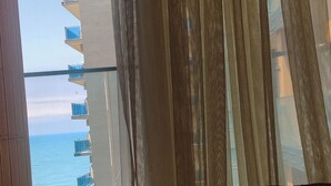 A bed with a laptop on it, a window with sheer curtains, and a view of a building with balconies and a body of water. - Apartment with Sea View in New Boulevard of Batumi (Batumi)