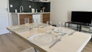 A dining table set with clear glassware and plates, a microwave above, and a TV in the background. - Apartment in Le Mans With Private Terrace (Le Mans)