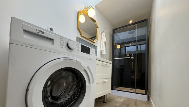 A compact laundry area with a front-loading washing machine, a mirror, and a glass-enclosed shower. - Apartment in Le Mans With Private Terrace (Le Mans)