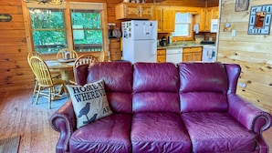 A cozy cabin interior with a leather sofa, wooden dining table, and a kitchen area.