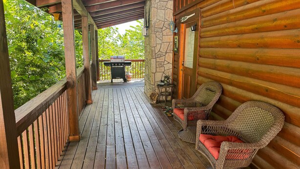 A wooden porch with wicker chairs and a barbecue grill.