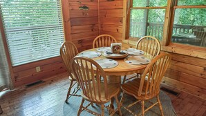 A wooden dining room with a round table and six chairs, each with a placemat.