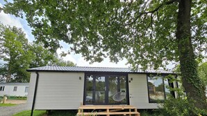 A mobile home with a tiled roof, a sliding glass door, and a small porch area. - Tiny House Drents-Friese Wold with terrace and parking lot (Hoogersmilde)