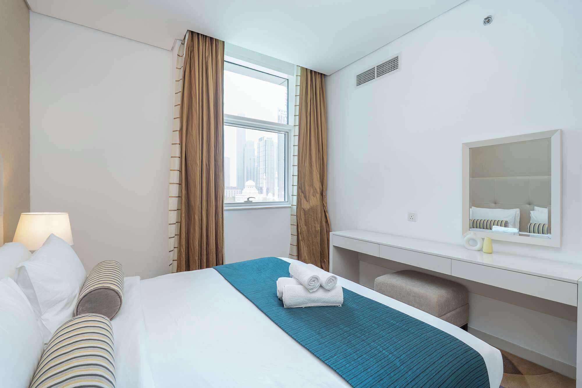 Habitación de hotel con cama, ventana con cortinas, escritorio con silla y espejo.