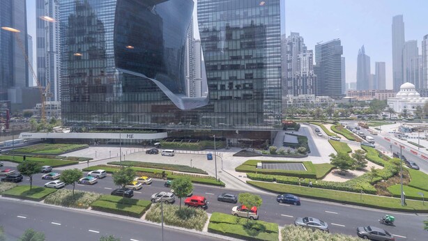 A modern urban landscape with high-rise buildings, a central plaza with greenery, and a busy road with vehicles.