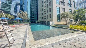 A modern building with a swimming pool, lounge chairs, and a clear view of surrounding skyscrapers.