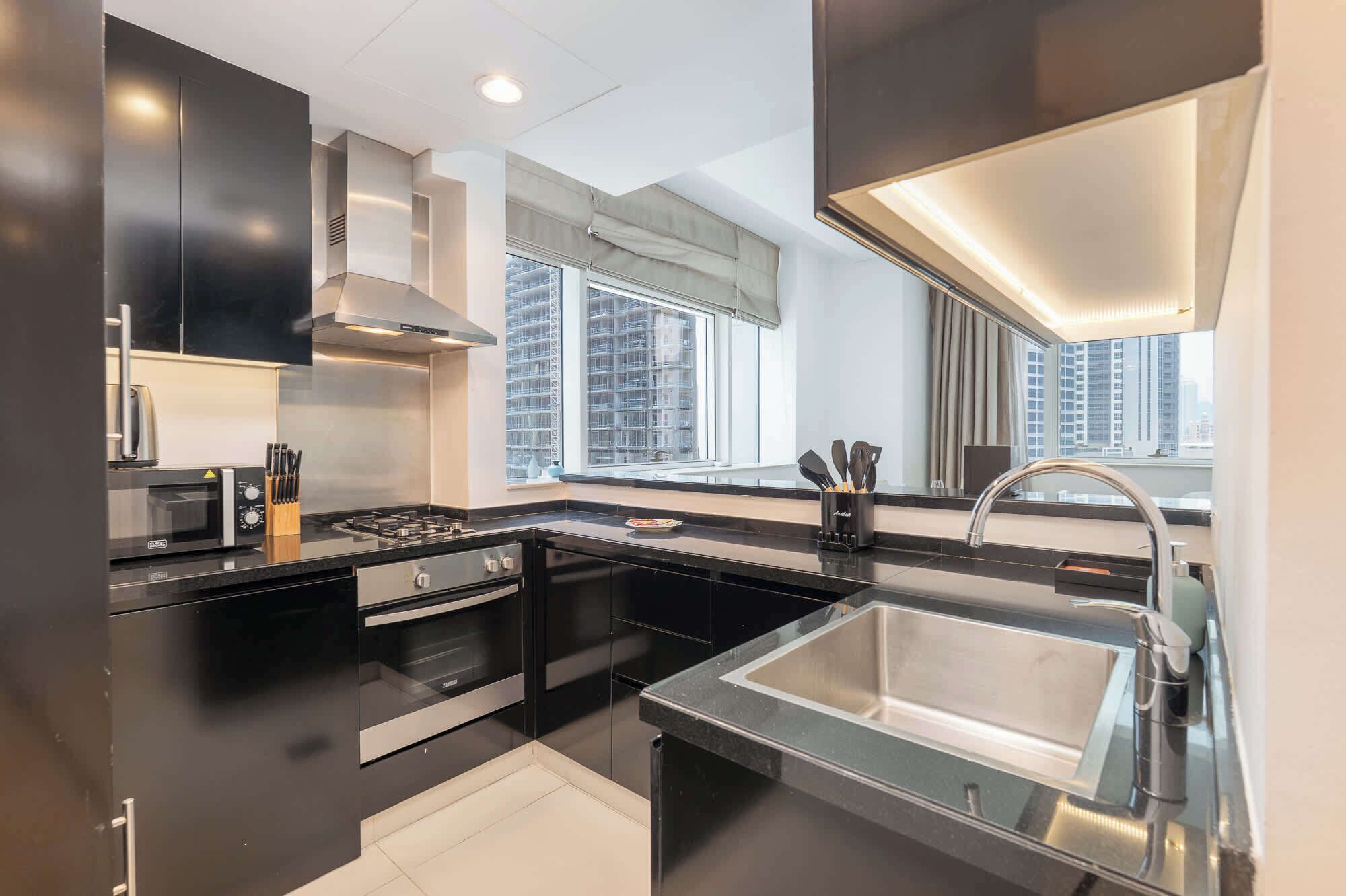 A modern kitchen with a stainless steel sink, black countertops, and a window with a city view.
