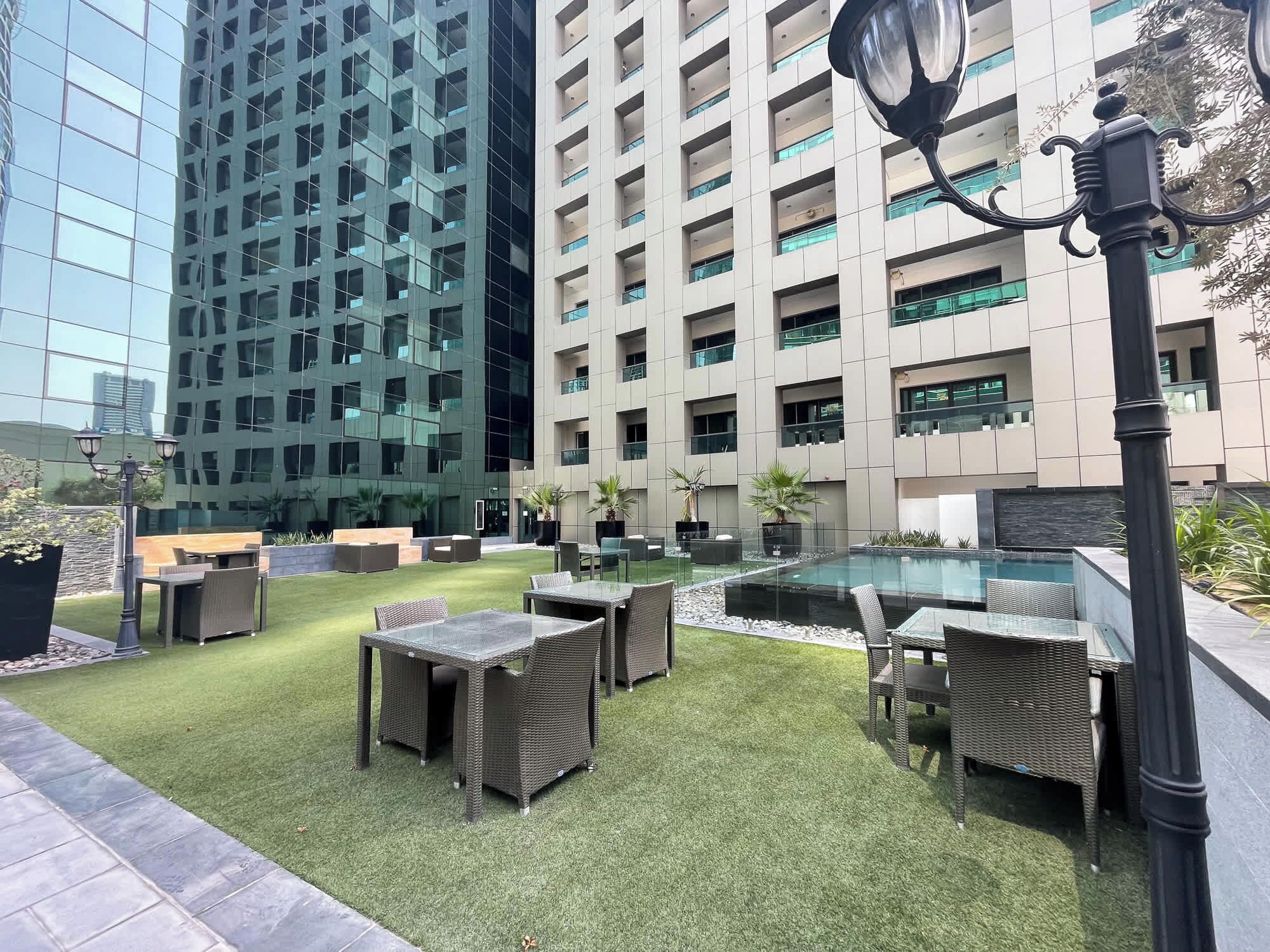 A rooftop garden with outdoor furniture, a pool, and modern buildings in the background.