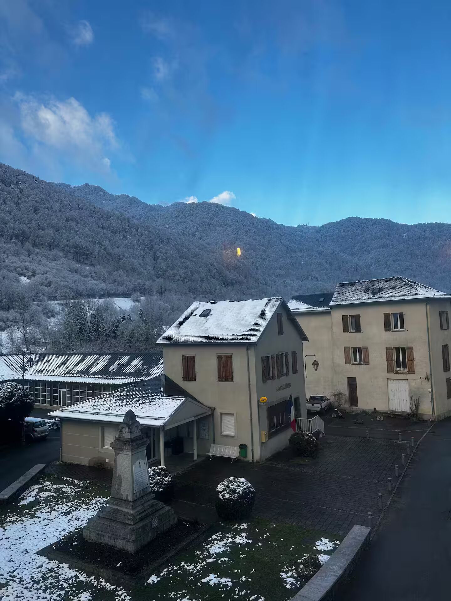 A building with a snow-covered roof, a courtyard, and a mountain in the background.