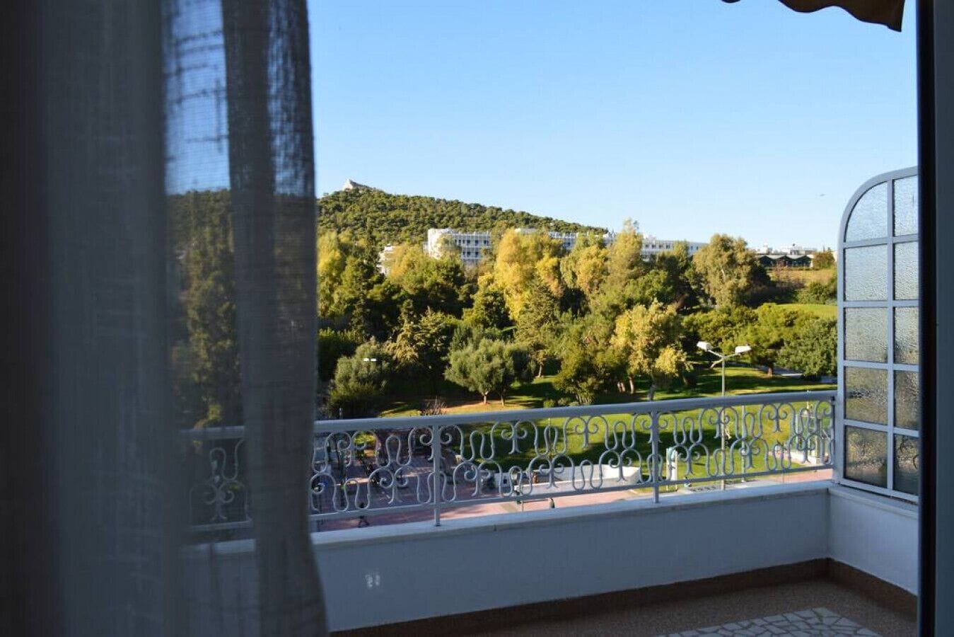 A balcony with a view of a park and buildings in the distance.