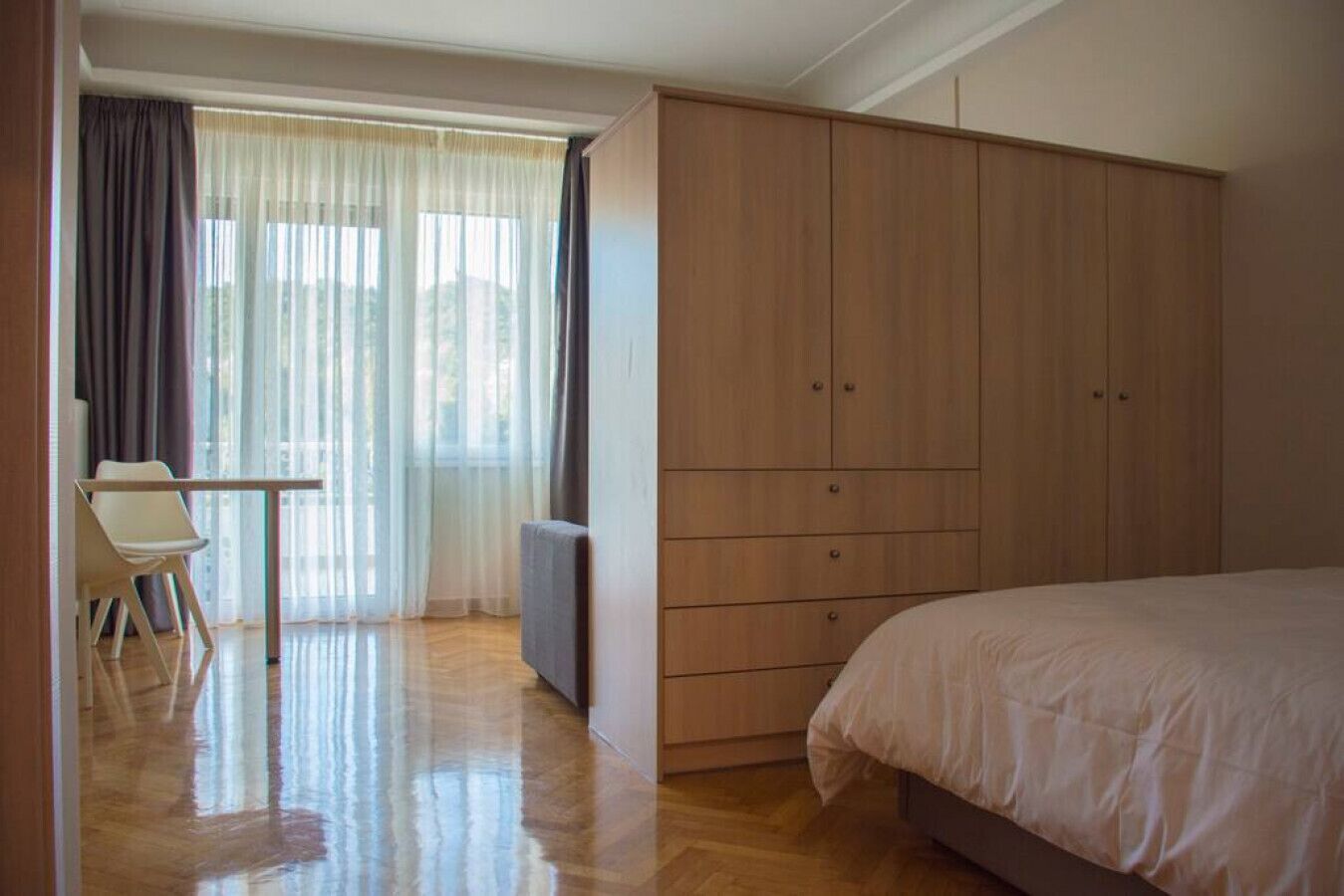 Een slaapkamer met een bed, een houten garderobe, een bureau en een stoel.
