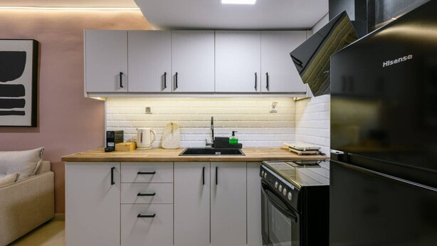 Cocina compacta con armarios blancos, un refrigerador negro y una encimera de madera.