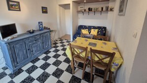 Una habitació senzilla amb un terra de pissos, una taula de dinar amb caires, un televisor sobre un moble i una prestatgeria.