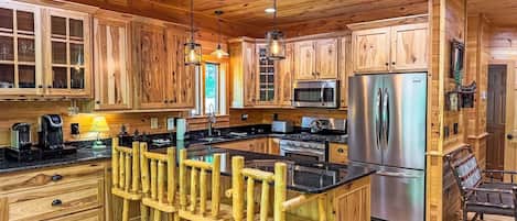 A spacious kitchen with wooden cabinets, a central island with stools, stainless steel appliances, and pendant lighting.