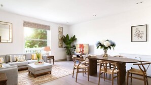 A spacious living room with a sofa, coffee table, and dining area with chairs. - Luxurious 3-Bedroom Notting Hill (Greater London)