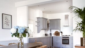 A modern kitchen with grey cabinets, a wooden dining table, and a vase of flowers. - Luxurious 3-Bedroom Notting Hill (Greater London)