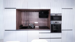 A compact kitchen with a built-in sink, a microwave, and a stove. - Urban Calm - Bright & Modern Stay (Le Mans)