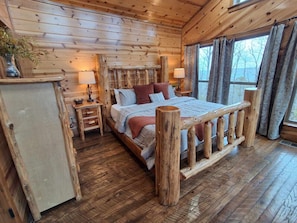 Une chambre située dans un chalet en rondins, avec un lit en bois, une table de chevet, une lampe et une fenêtre avec des rideaux.