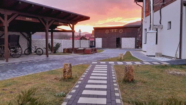 A covered outdoor area with a paved walkway leading to a building with a wooden facade and a sign reading "DURAS." - Vidra Dacica (Vidra)