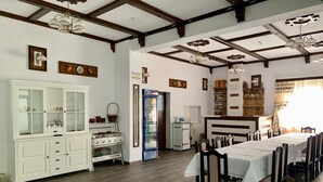 A dining area with a long table, chairs, a cabinet, a refrigerator, and a kitchen area with a stove. - Vidra Dacica (Vidra)