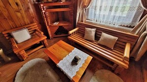 A cozy cabin interior with a wooden sofa, a small table, and a window with lace curtains. - Vidra Dacica (Vidra)