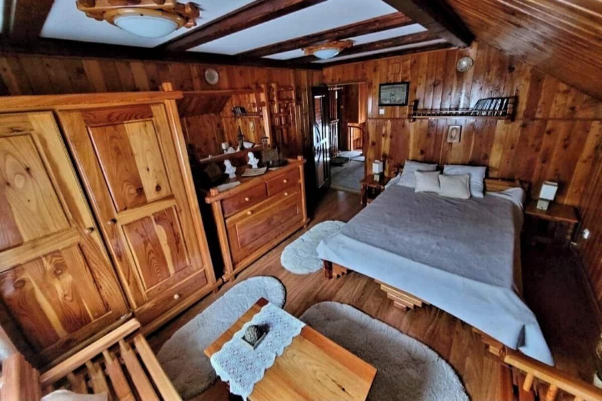 A wooden cabin interior with a bed, dresser, and a small table.