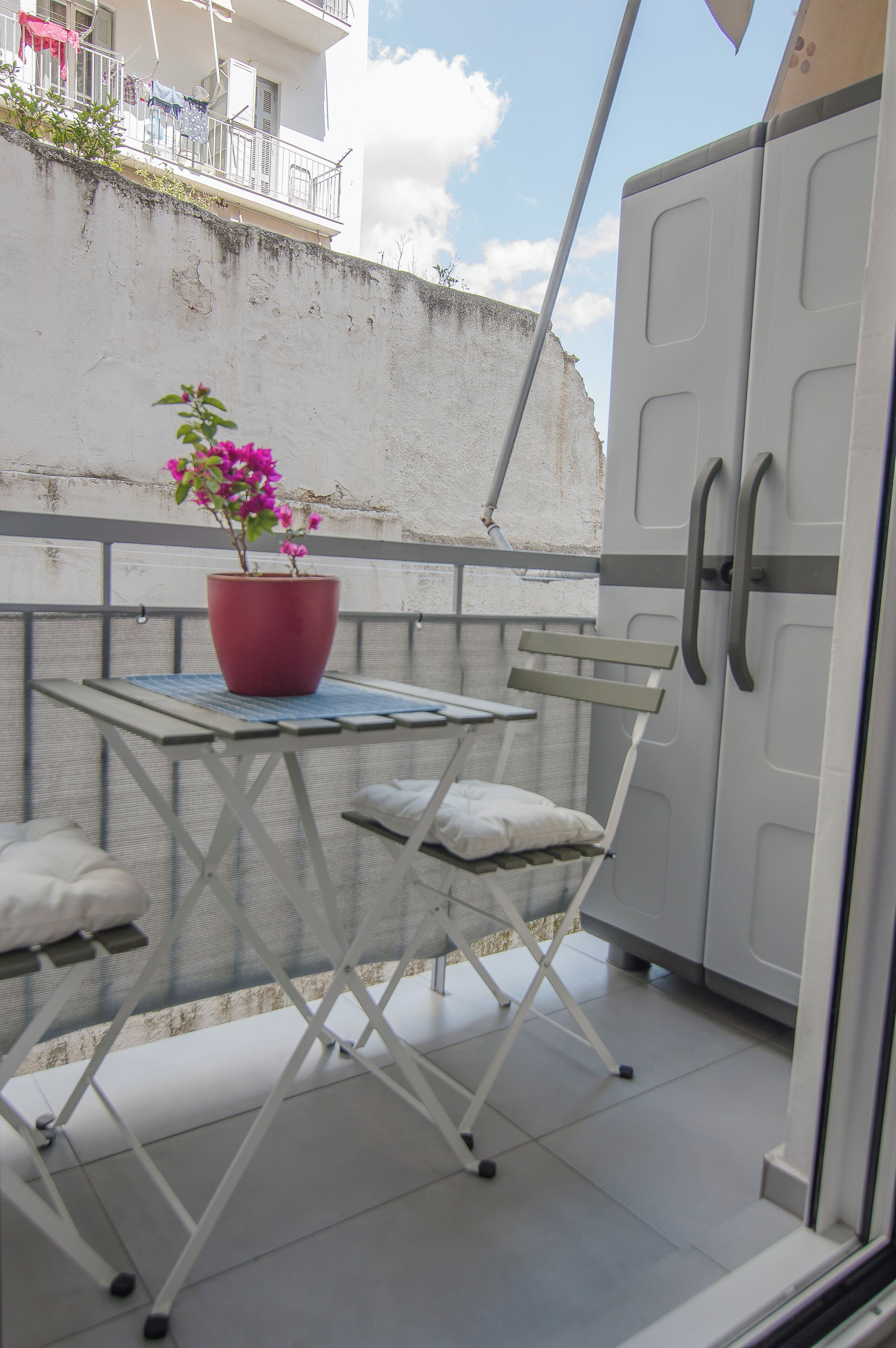 A balcony with a table, a chair, a potted plant, and a wardrobe.
