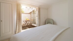 Une chambre avec un grand lit, une chaise et une petite table sur laquelle se trouvent un vase et des fruits.