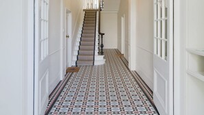 Un couloir avec des carreaux de sol à motifs, un escalier doté d’une rampe et un lustre.