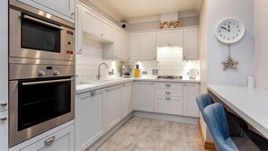 A modern kitchen with white cabinetry, a built-in oven, a sink, and a clock on the wall.