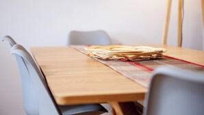 A wooden table with a red and white placemat, a stack of wooden chopsticks, and two grey chairs.