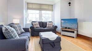 A living room with a grey sofa set, a flat-screen TV, and a white radiator.