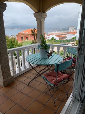 Een balkon met een tafel en stoelen, een bloempot en uitzicht op gebouwen en water.