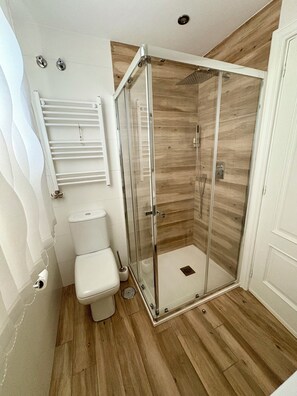 Een moderne badkamer met een douchecabine van glas, een toilet en een handdoekrek.