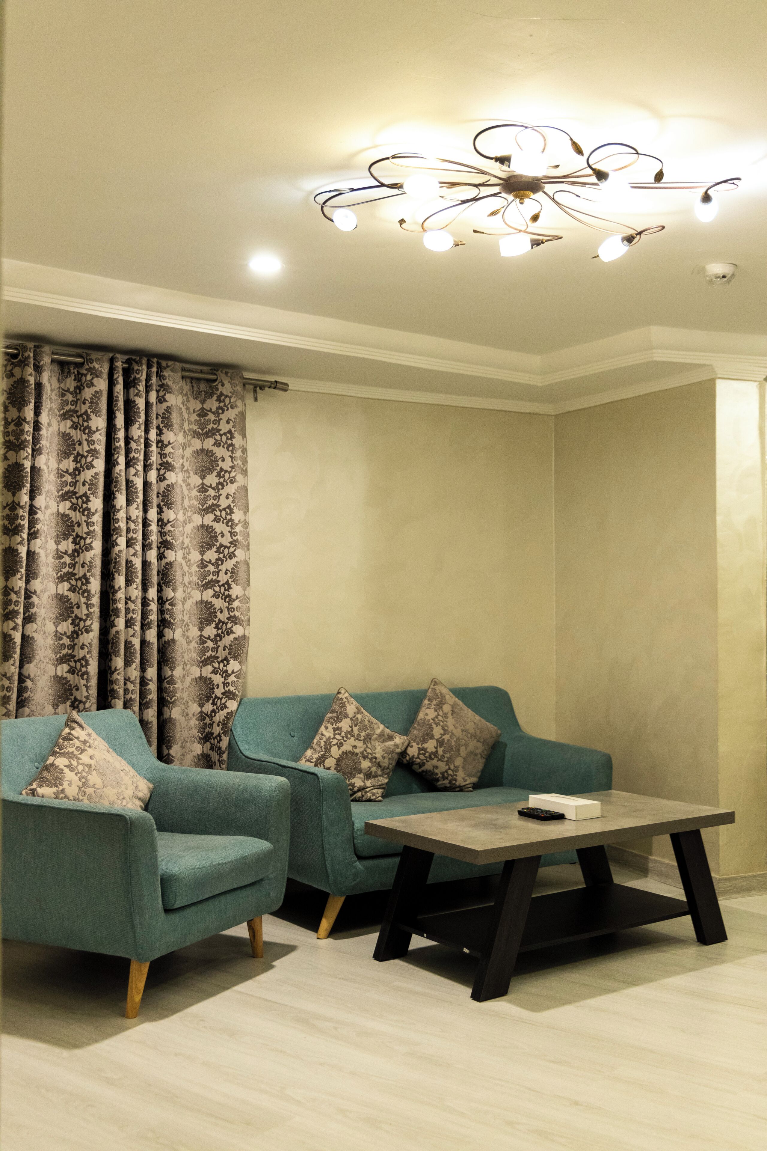 Una sala de estar con dos sillones turquesa, una mesa de centro y una cortina estampada.