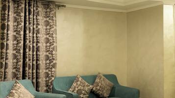 Una sala de estar con dos sillones turquesa, una mesa de centro y una cortina estampada.
