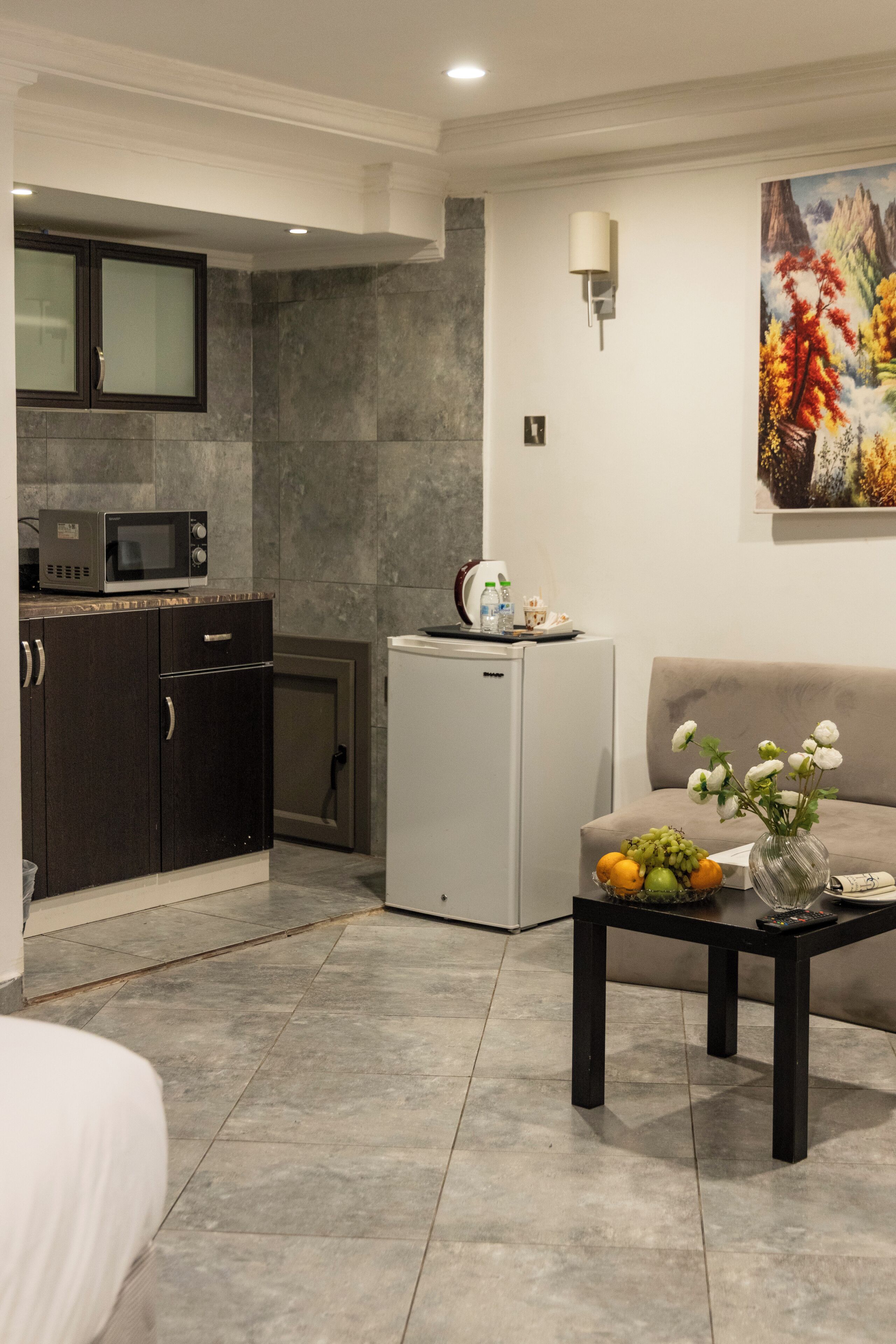 Una cocina moderna con armarios oscuros, un refrigerador blanco y un microondas. Hay una zona de comedor con un sofá y una mesa con fruta.