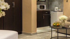 A modern hotel room with a bed, a round coffee table with fruit and flowers, a kitchenette with a microwave, and a dark wooden wardrobe. - Salmiya Grand Hotel (Salmiya)