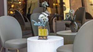 A seating area with two chairs and a small table, a menu stand, and a decorative vase with flowers. - Salmiya Grand Hotel (Salmiya)