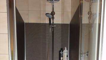 Cabina doccia con pareti in vetro, soffione a mano, spazzola esfoliante e ripiano con due flaconi di shampoo.