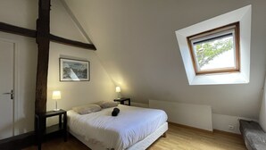 A bedroom with a sloped ceiling, a bed with white bedding, two bedside lamps, a framed picture on the wall, and a window with a view of greenery. - Relaxing Nature Stay in Thoree-les-pins (Thorée-les-Pins)