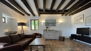 A living room with a stone floor, a sofa, a table, a cabinet, a TV, and a painting on the wall. - Relaxing Nature Stay in Thoree-les-pins (Thorée-les-Pins)