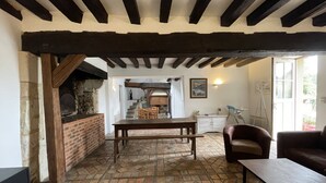 A rustic interior with exposed wooden beams, a brick fireplace, a tiled floor, and a dining area with a table and chairs. - Relaxing Nature Stay in Thoree-les-pins (Thorée-les-Pins)