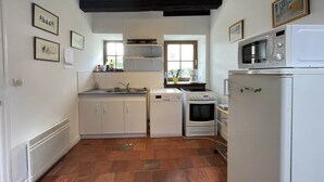 A compact kitchen with white cabinets, a sink, a dishwasher, an oven, and a microwave. There are framed pictures on the walls and a window with a view. - Relaxing Nature Stay in Thoree-les-pins (Thorée-les-Pins)