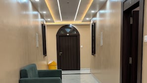A hallway with a marble floor, a green sofa, and a door with a sign. - Hotel Anu  (Phulpur)